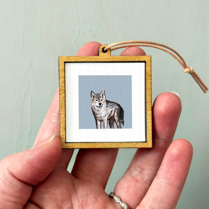 A person's hand holding a small wooden frame containing a picture of a wolf.