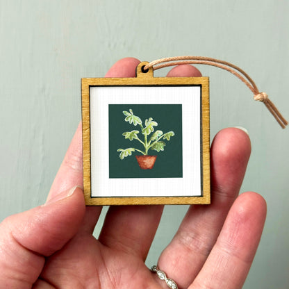 A hand holding a small wooden frame containing a framed picture of a potted plant.