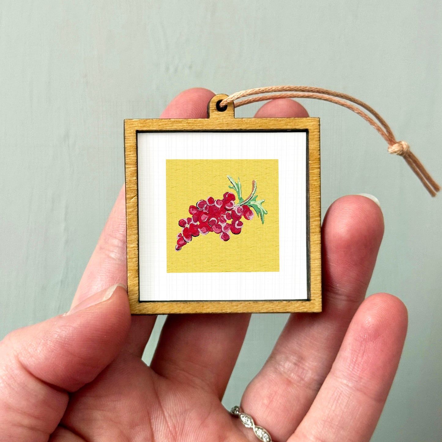 A hand holding a small wooden frame containing a framed image of red grapes.