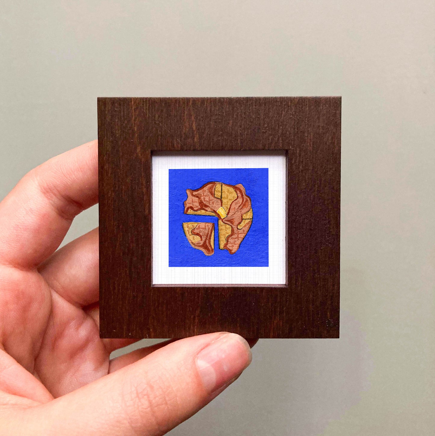 A hand is holding a small square frame containing a painting of a bear.