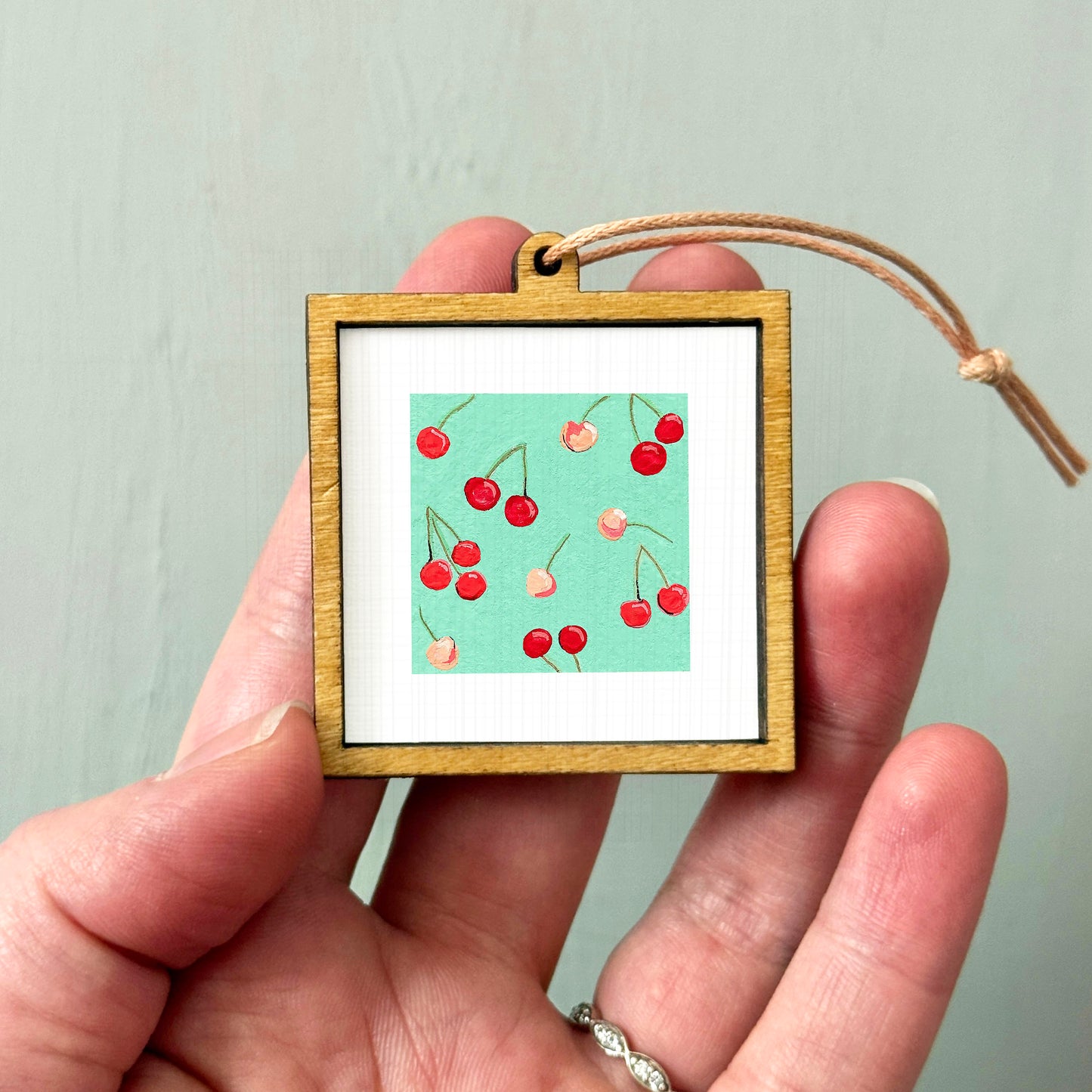 A hand holding a small wooden frame containing a picture of cherries.