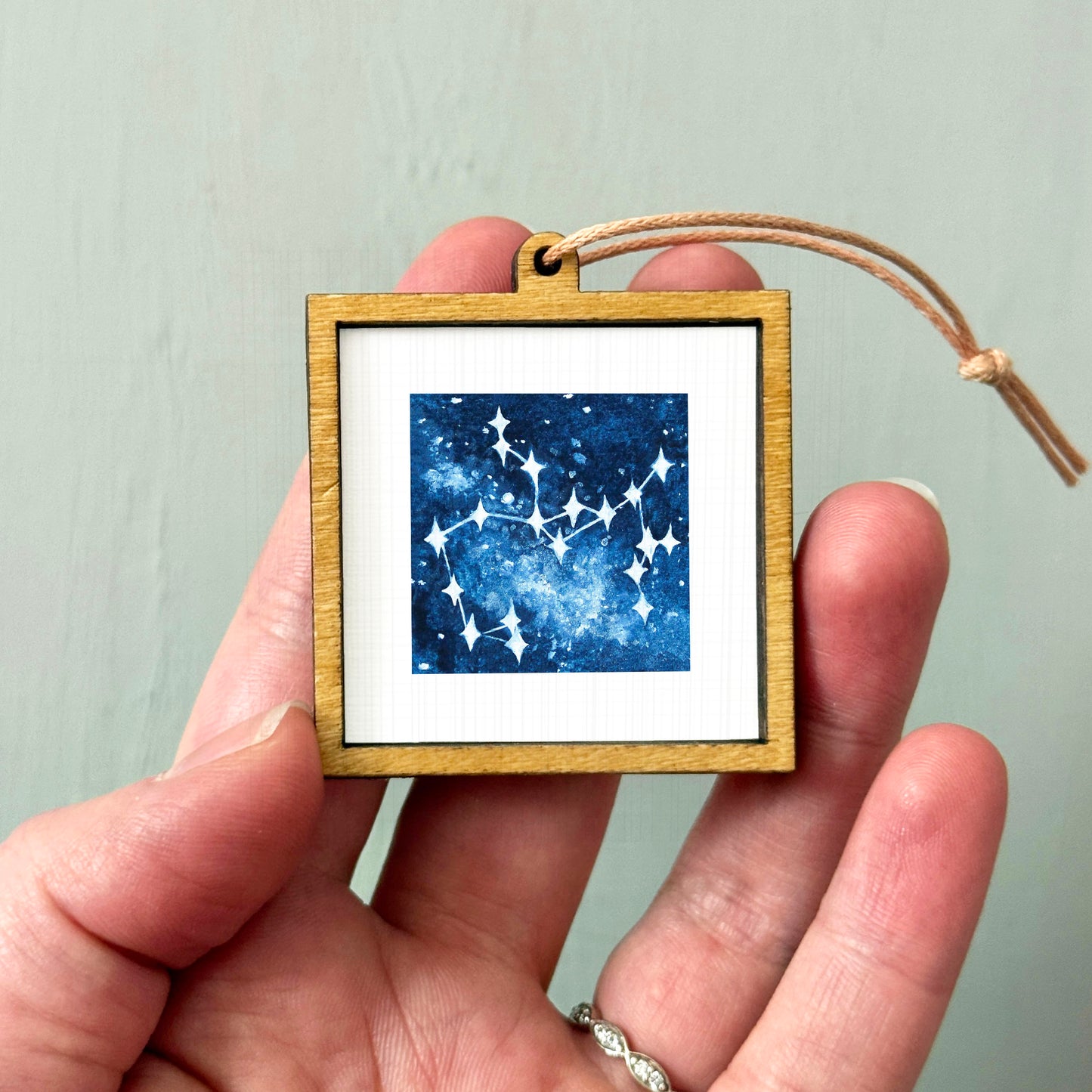 A hand holding a small wooden frame containing a framed image of a starry night sky.