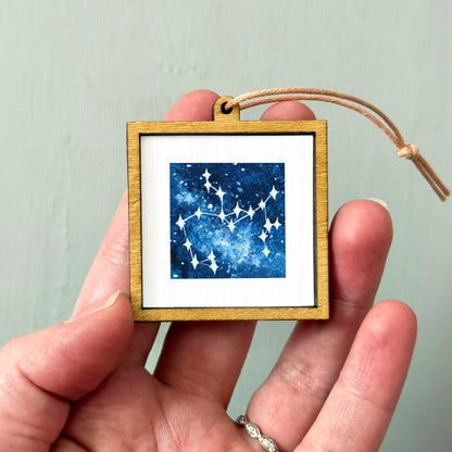 A hand holding a small wooden frame containing a framed image of a starry night sky.