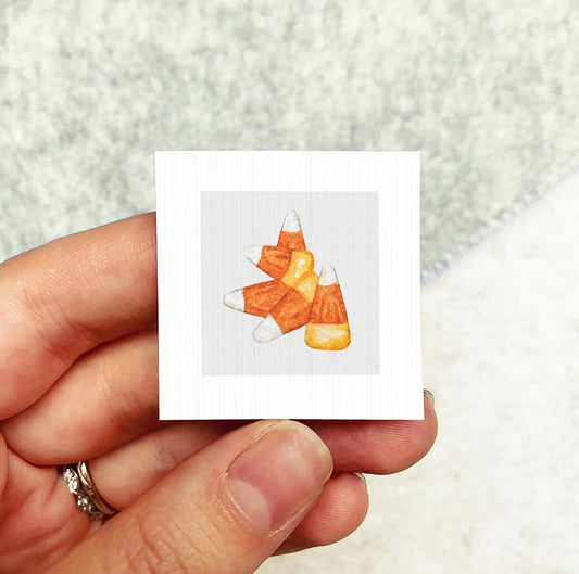 A hand holding a small square card with an illustration of candy corn on it.