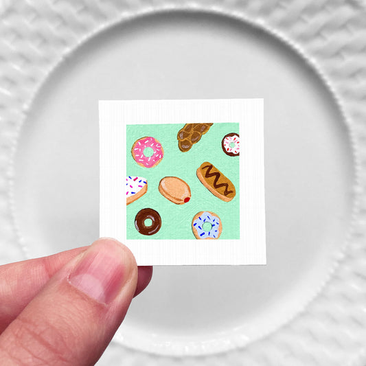 A hand is holding a small square card with a vibrant illustration of various donuts on it.