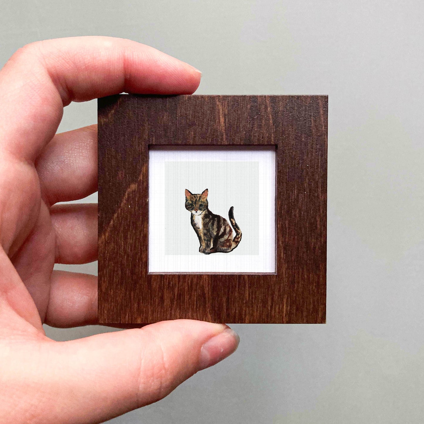 A hand is holding a small wooden frame containing a picture of a cat.