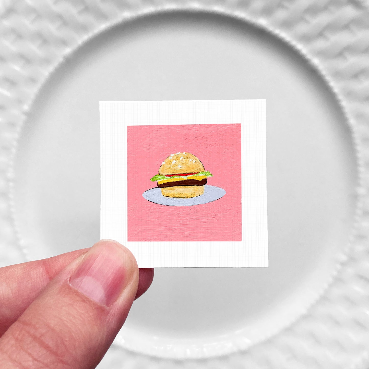 A hand is holding a small square with a picture of a hamburger on it.