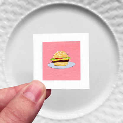 A hand is holding a small square with a picture of a hamburger on it.