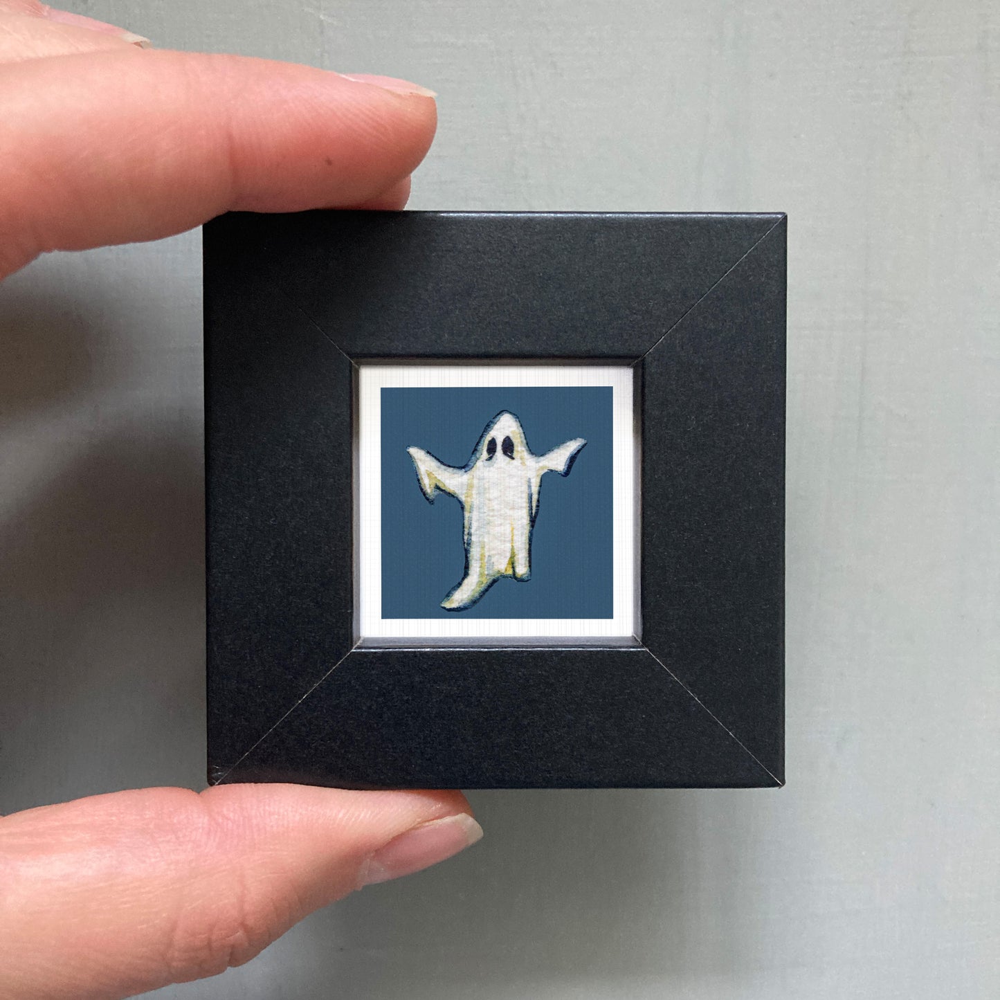 A hand is holding a small black frame containing a picture of a ghost.