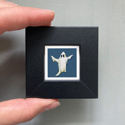 A hand is holding a small black frame containing a picture of a ghost.