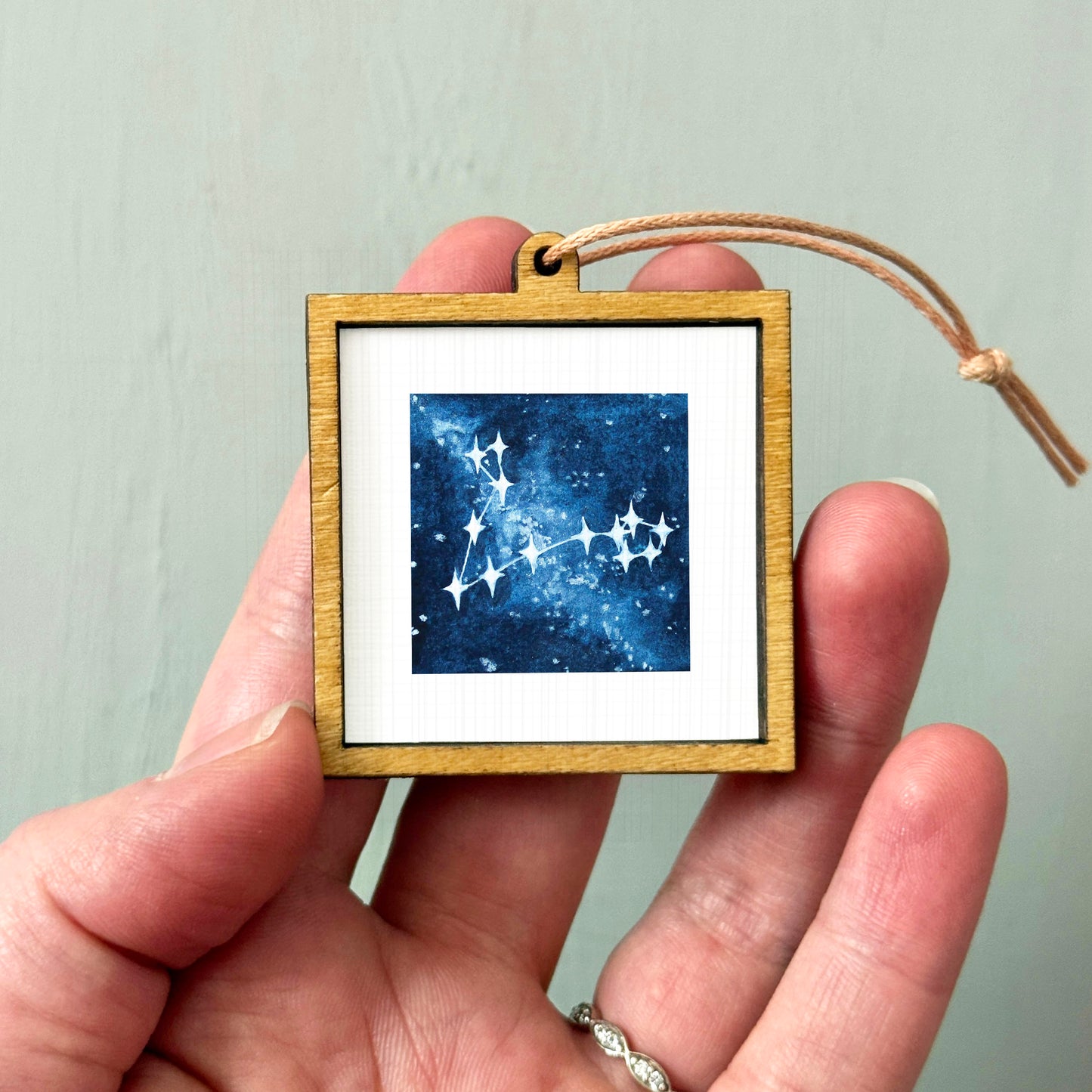 A hand holding a small wooden frame containing a framed image of a starry night sky.
