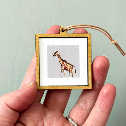 A person's hand holding a small wooden frame containing a picture of a giraffe.