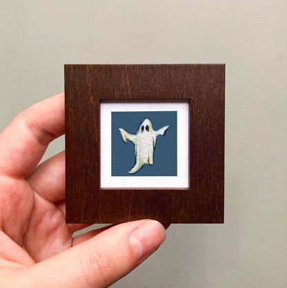 A hand is holding a small wooden frame containing a picture of a ghost.