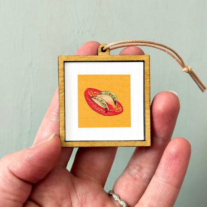 A hand holding a small wooden frame containing a framed image of a red bowl with a yellow interior.