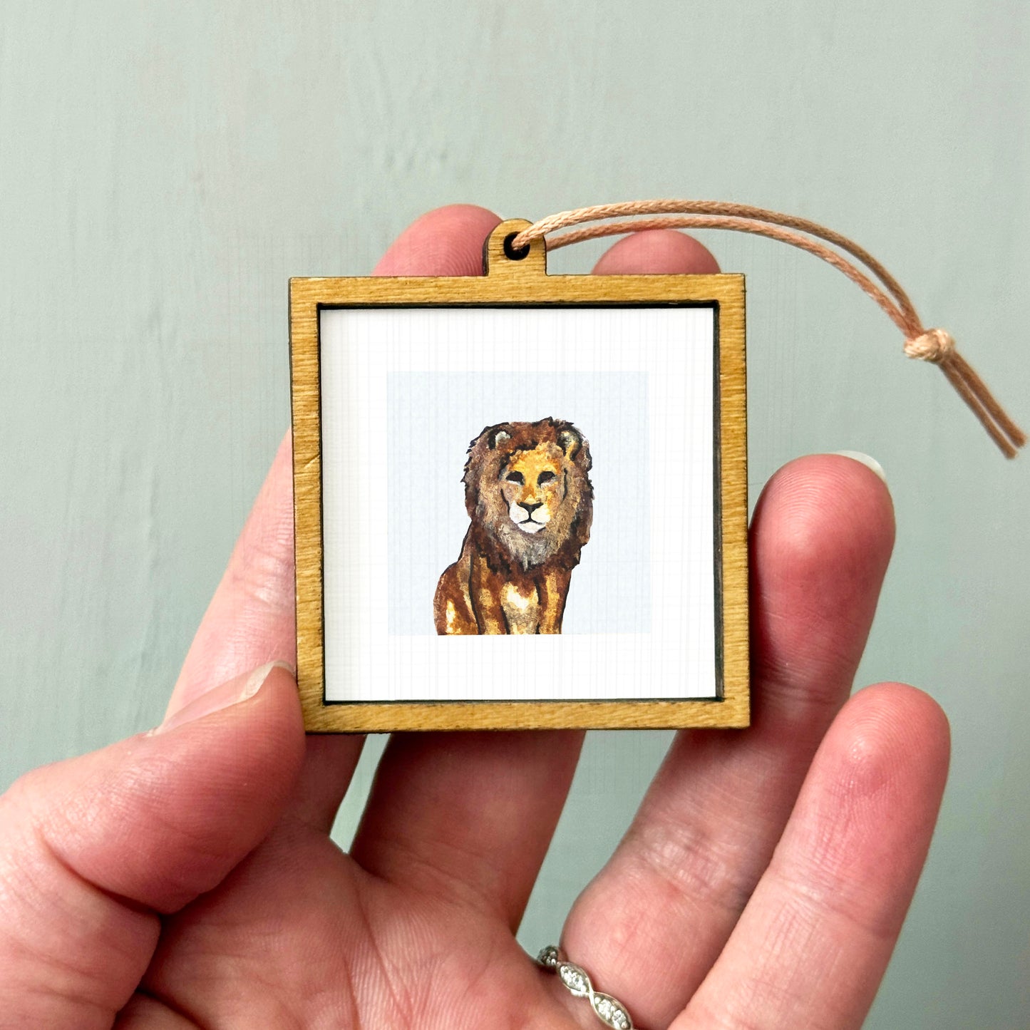 A person's hand holding a small wooden frame containing a picture of a lion.