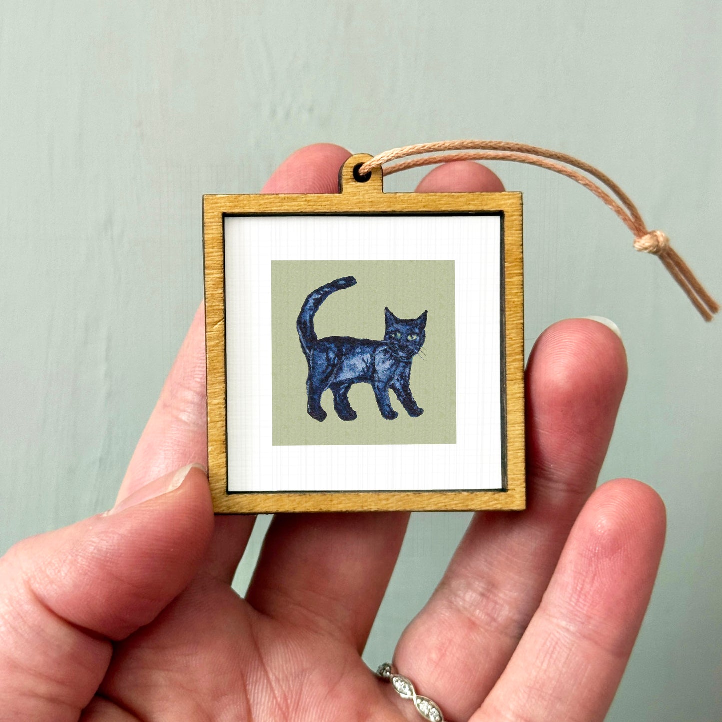 A hand holding a small wooden frame containing a picture of a black cat.