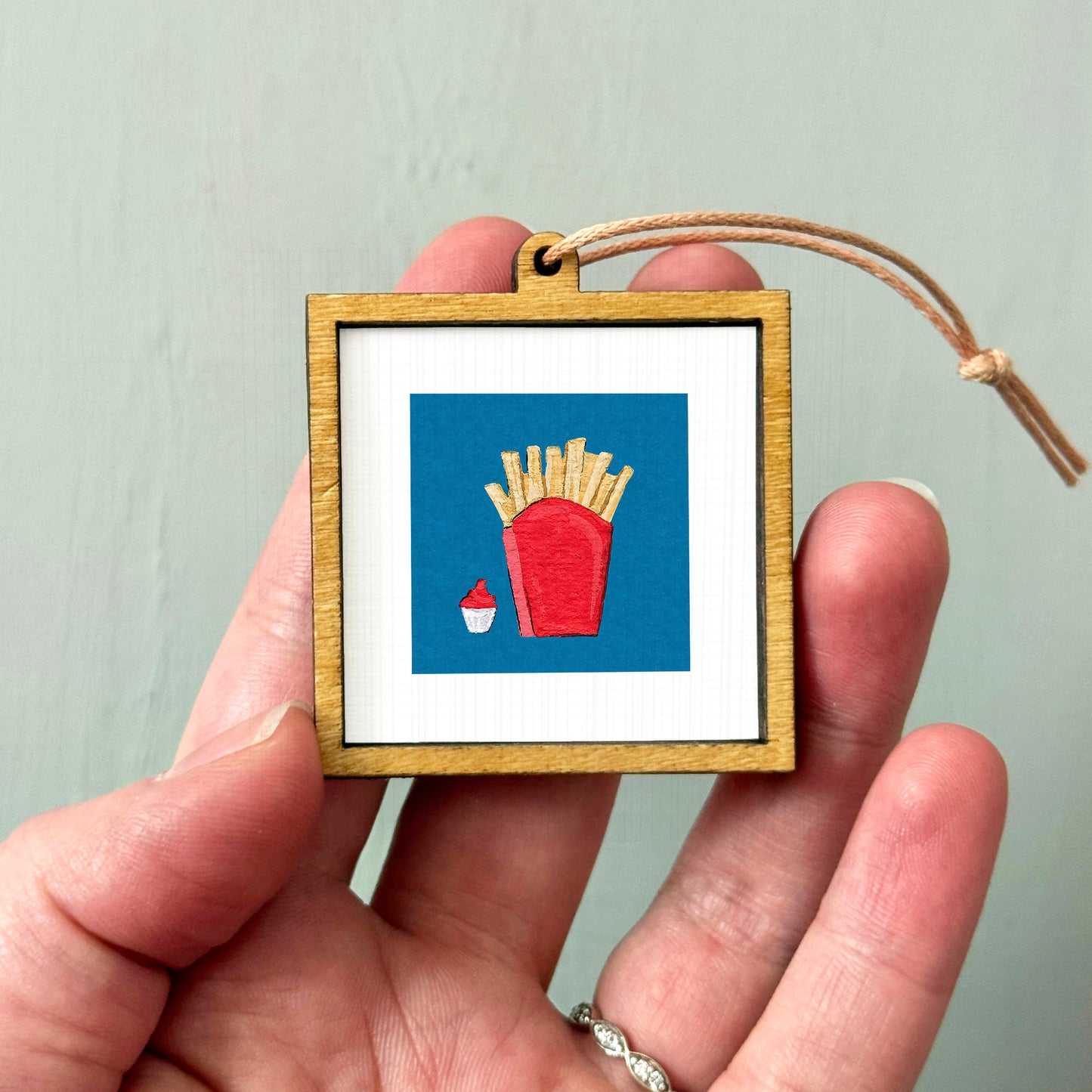 A hand holding a small wooden frame containing a picture of french fries and a cupcake.