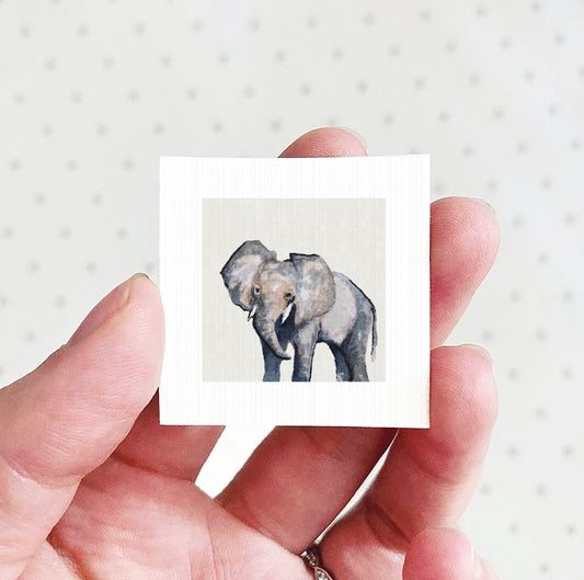 A hand holding a small square picture of an elephant.