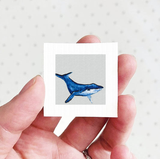 A hand holding a small square picture of a blue whale.