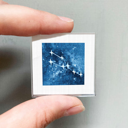 A hand is holding a small square-shaped object with a blue background and white stars, which appears to be a piece of art or a decorative item.