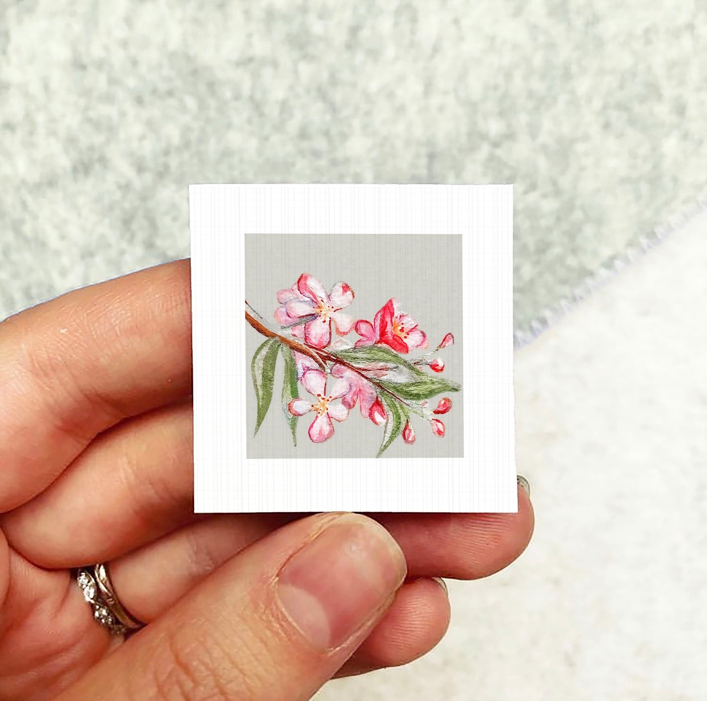 A hand holding a small square card with a floral design on it.