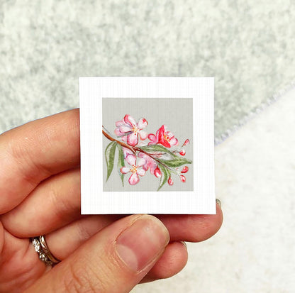 A hand holding a small square card with a floral design on it.