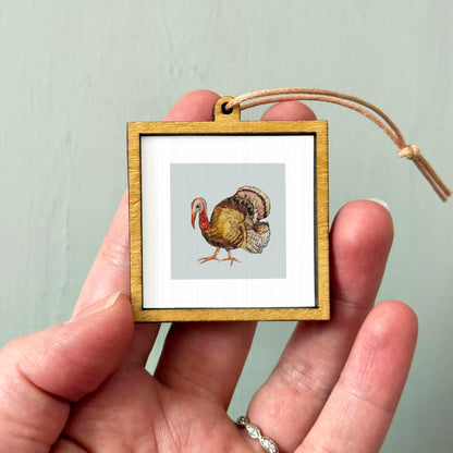 A person's hand holding a small wooden frame containing a picture of a turkey.