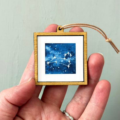 A hand holding a small wooden frame containing a framed image of a starry night sky.