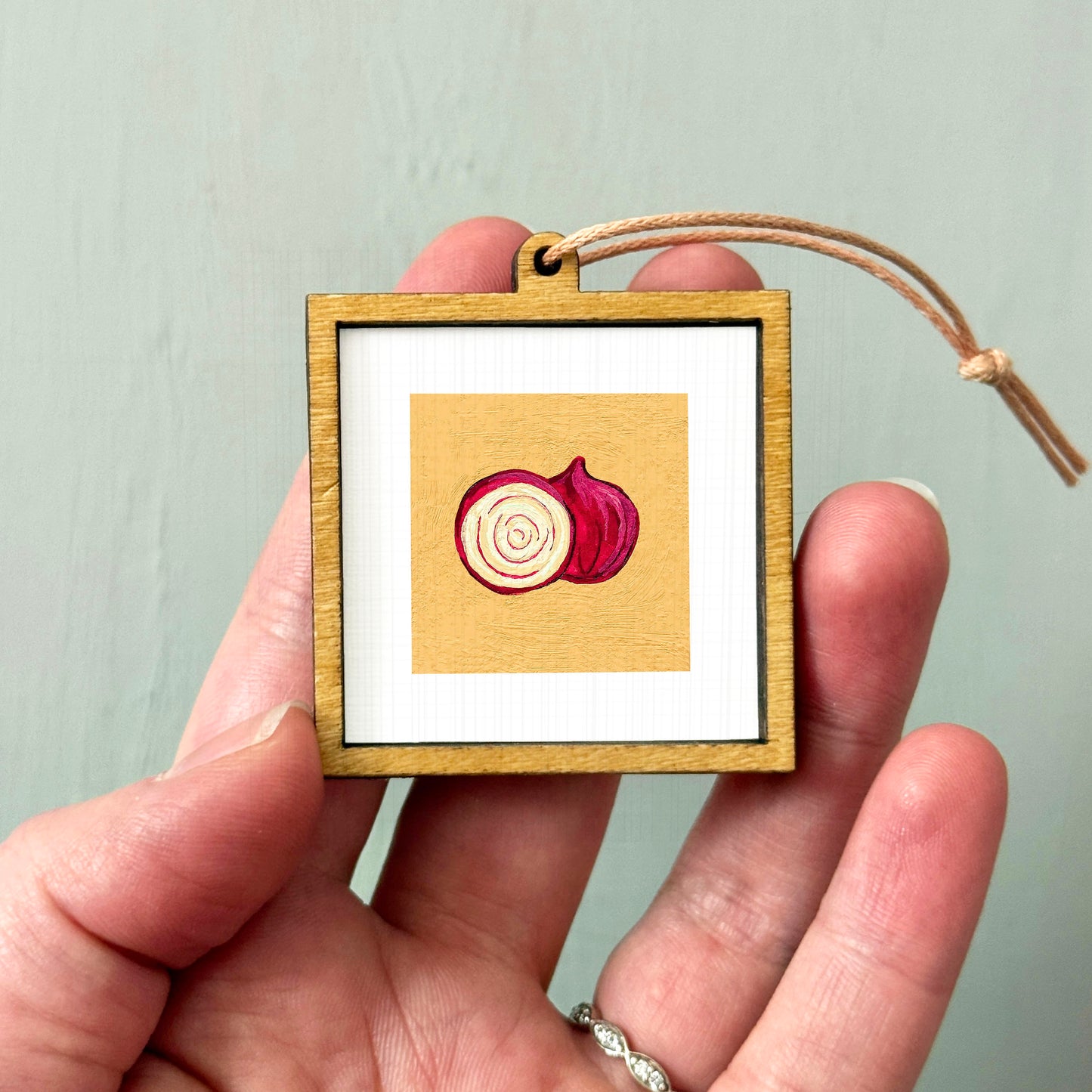 A hand holding a small wooden frame with a picture of a red onion inside it.