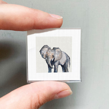 A person's hand is holding a small square picture of an elephant.