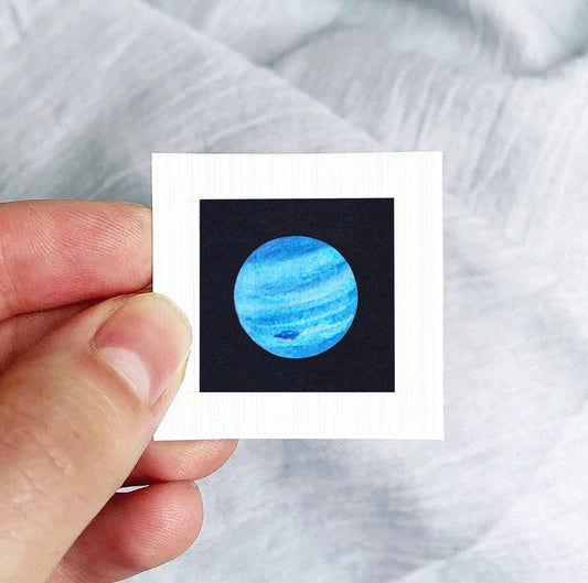 A hand is holding a small square-shaped paper with a picture of a blue planet on it.