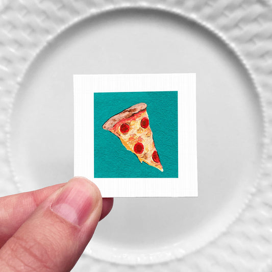 A hand is holding a small square with a picture of a slice of pizza on it, against a white plate background.