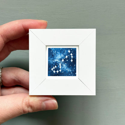 A hand is holding a small white square frame containing a blue and white starry night sky design.