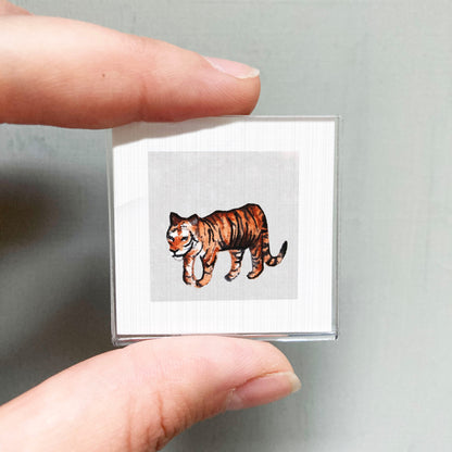 A person's hand is holding a small square picture of a tiger.