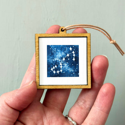 A hand holding a small wooden frame containing a picture of a starry night sky.