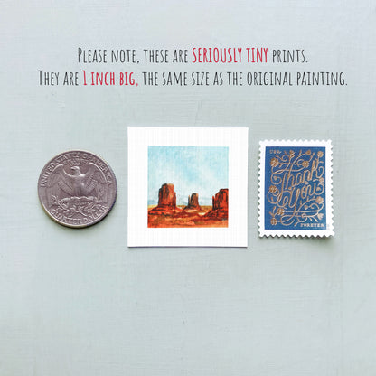 three small prints: a quarter, a square print of a desert landscape, and a blue postage stamp with gold lettering.