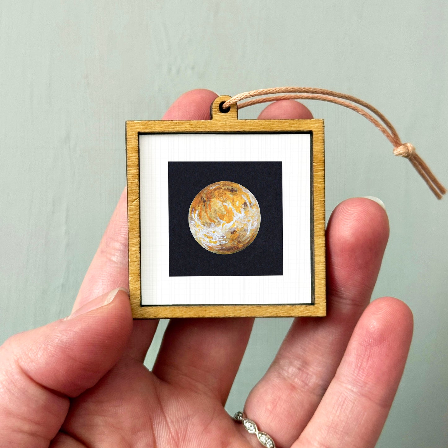 A hand holding a small wooden frame containing a picture of a planet.