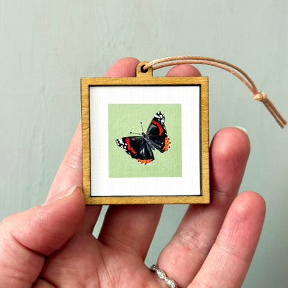 A hand holding a small wooden frame containing a framed image of a butterfly.