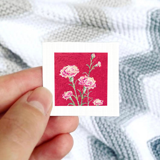 A hand is holding a small square card with a vibrant red background featuring a floral design.