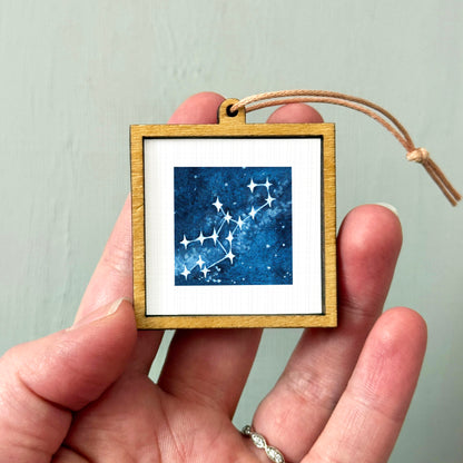 A hand holding a small wooden frame containing a framed image of a starry night sky.