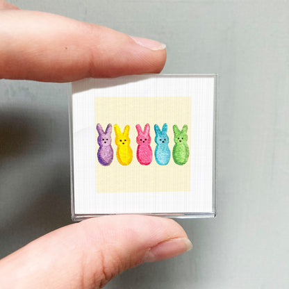 A person's hand is holding a small square with a colorful illustration of four pea pods in different colors.