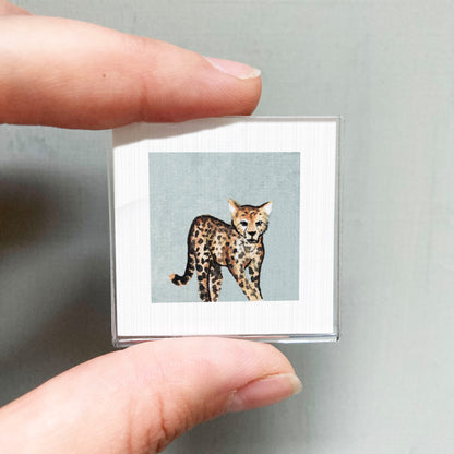 A person's hand is holding a small square picture of a cheetah, which is a type of feline.