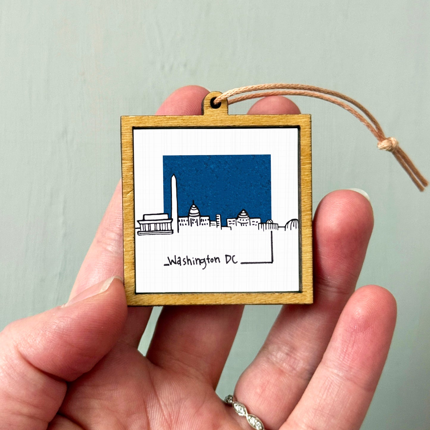A hand holding a small wooden frame with a picture of Washington, D.C. inside it.