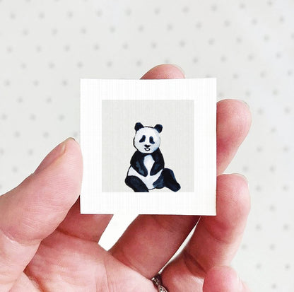 A hand holding a small square picture of a panda bear.