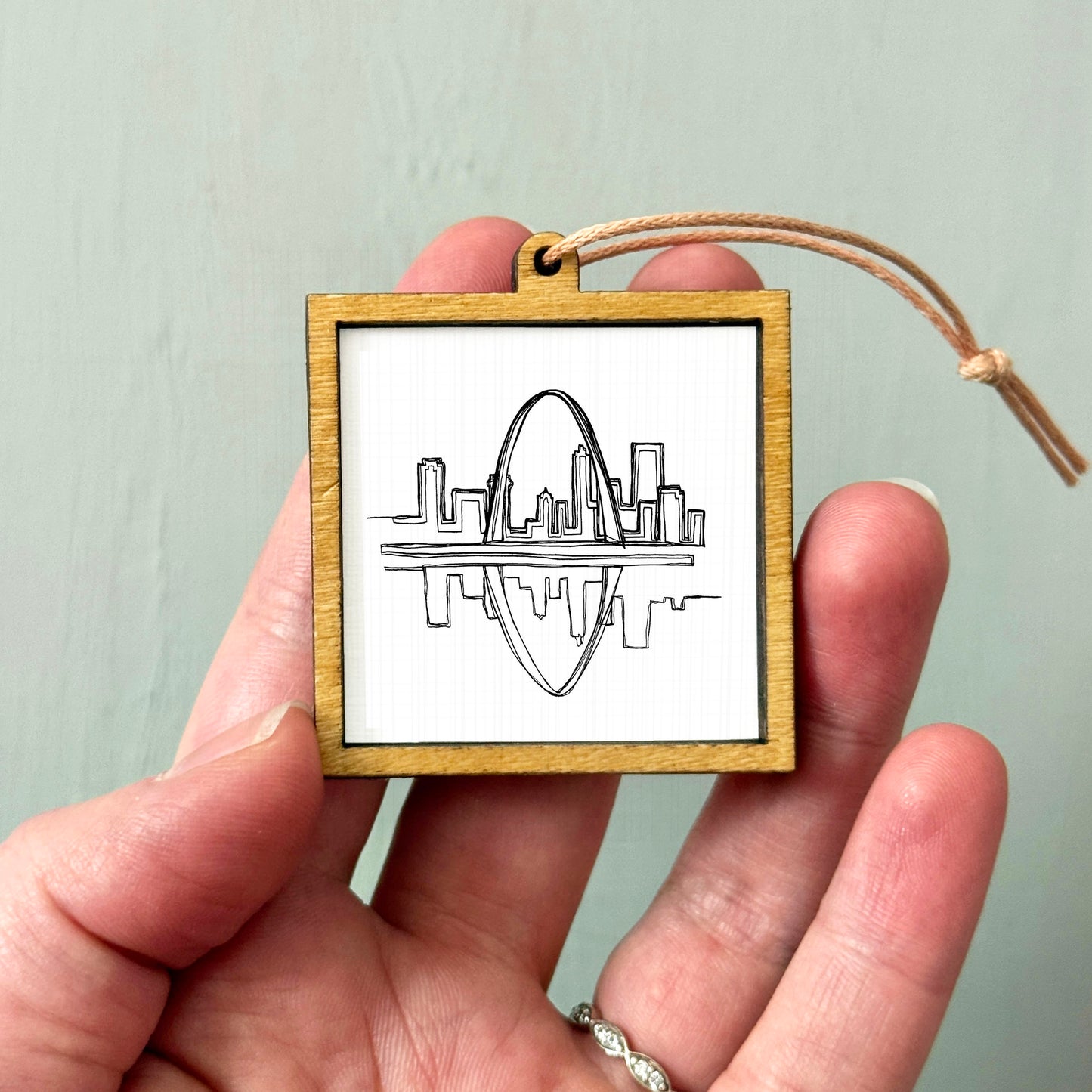 A hand holding a small wooden frame with a drawing of a city skyline inside it.