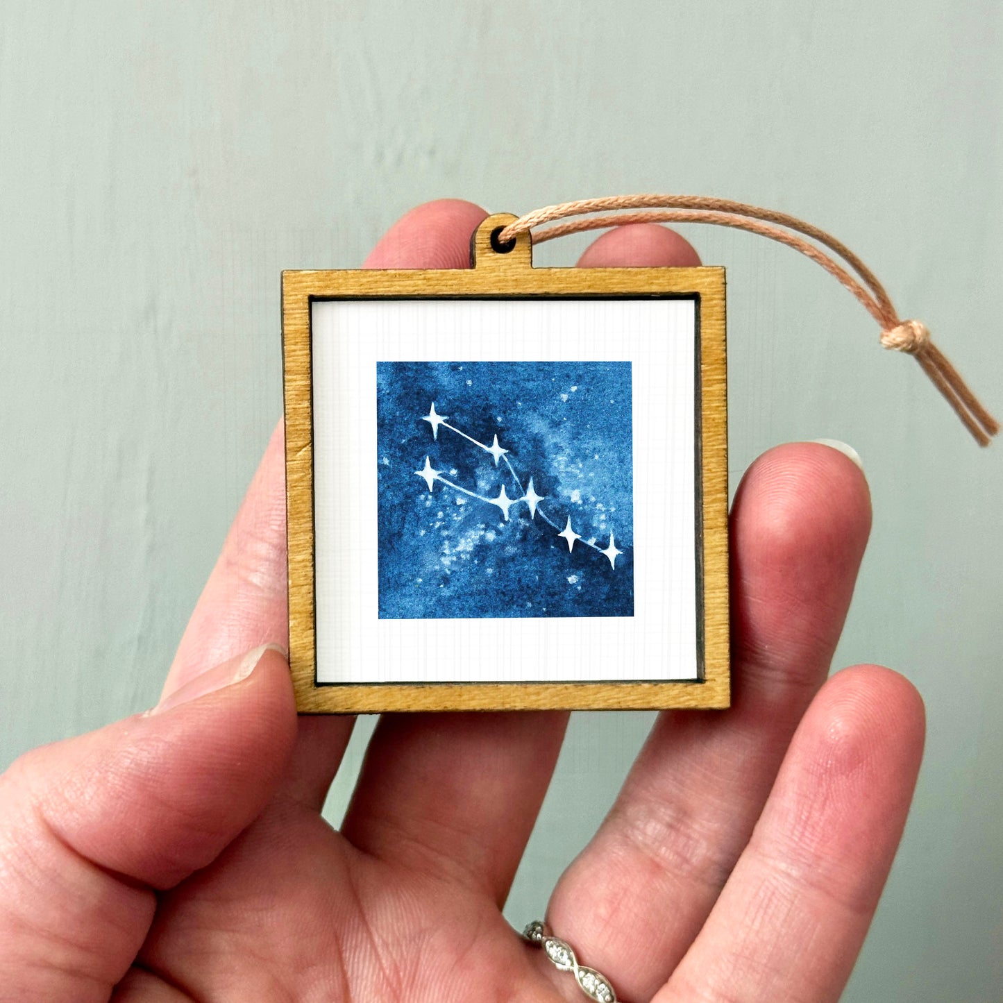 A hand holding a small wooden frame containing a framed image of a starry night sky.