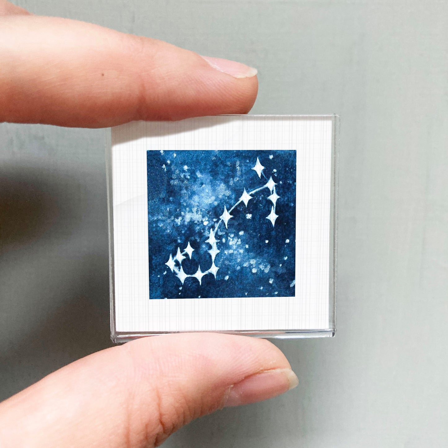 A person's hand holding a small square-shaped object with a blue and white starry night sky design on it.
