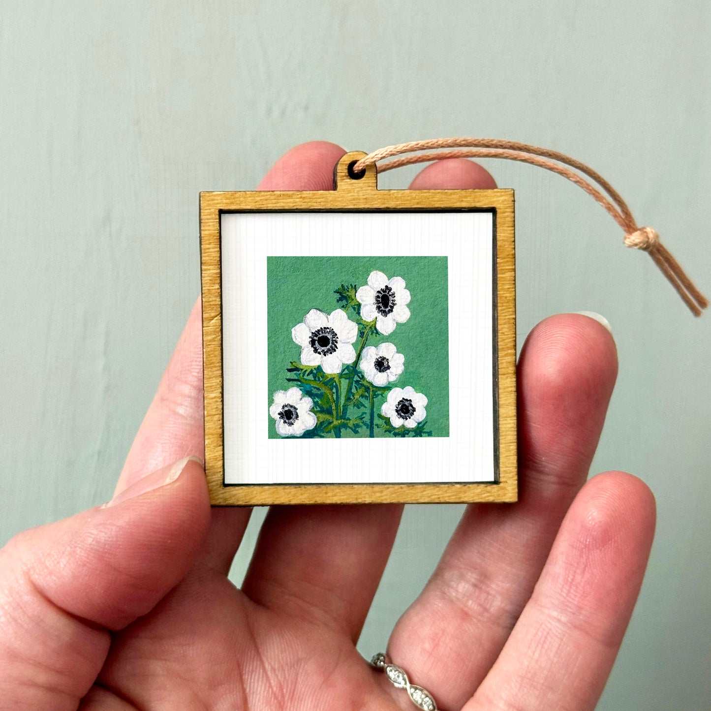 A hand holding a small wooden frame containing a picture of white flowers against a green background.