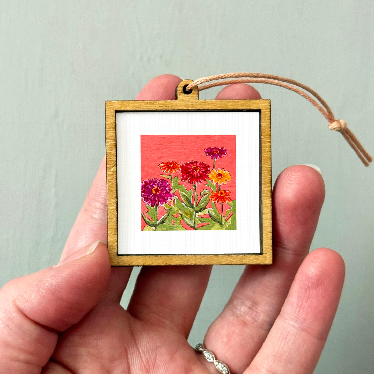 A hand holding a small wooden frame containing a framed painting of colorful flowers.