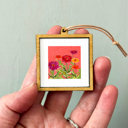 A hand holding a small wooden frame containing a framed painting of colorful flowers.
